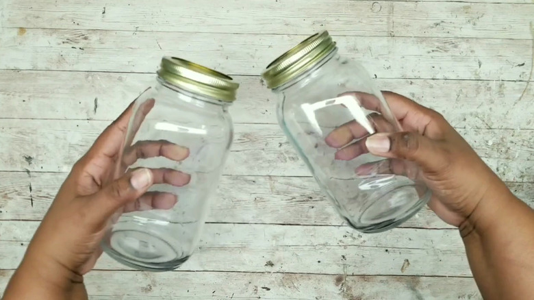 Hands holding two old mason jars above a wood surface