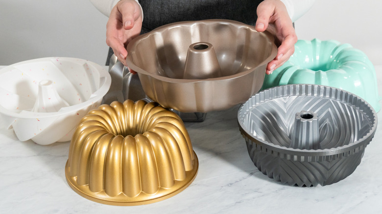 Hands hold one Bundt pan with other colors/styles of pans scattered around