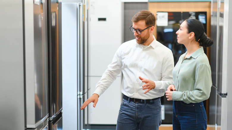 A man and woman looking at refrigerators at store