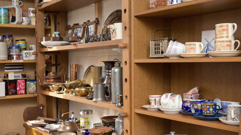 cups, saucers, pans, and other items on the shelves at a thrift store