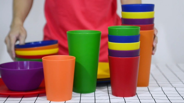 Person in red shirt standing behind stacks of colorful plastic reusable cups and dinnerware set