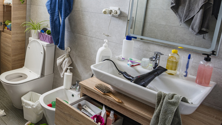 Cluttered bathroom countertop with open drawers and scattered hair products and teeth cleaning supplies