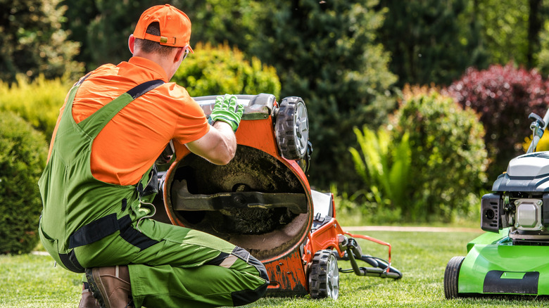 A person in uniform kneeling down to work on a lawn mower.