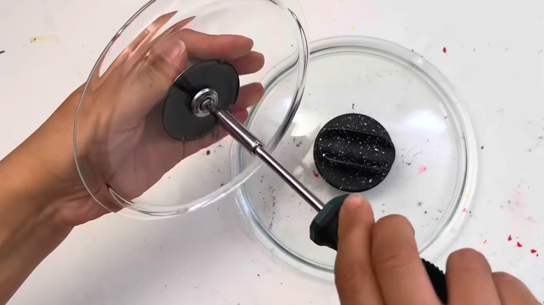 Person unscrewing pot lid handle for upcycling DIY idea above white countertop
