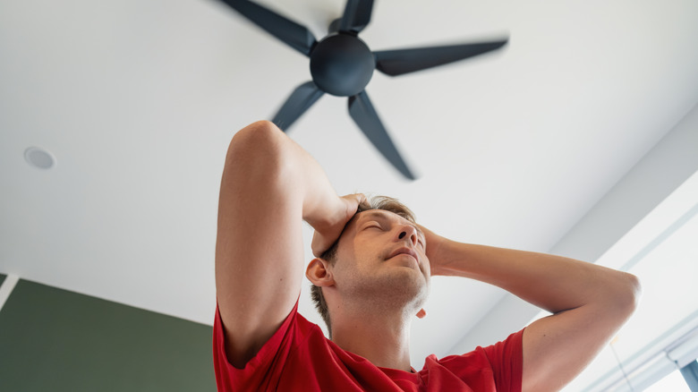 A tired man standing underneath a ceiling fan