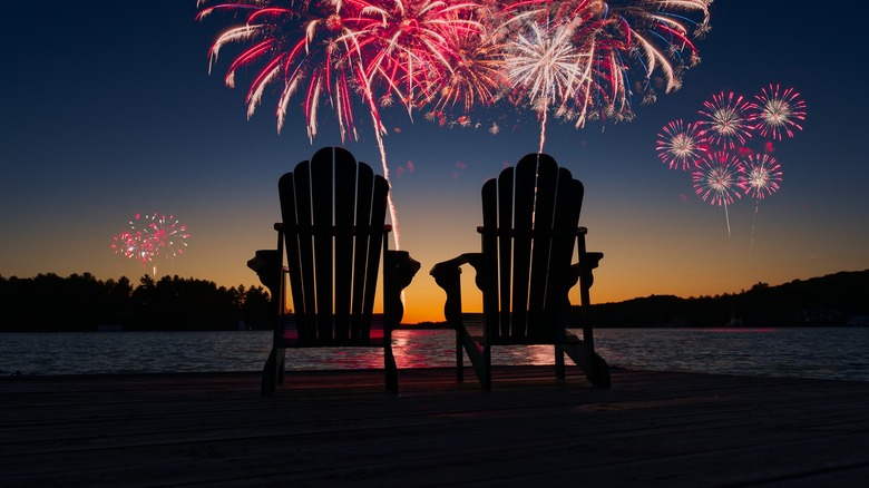 Two chairs in front of a lake with fireworks in the background