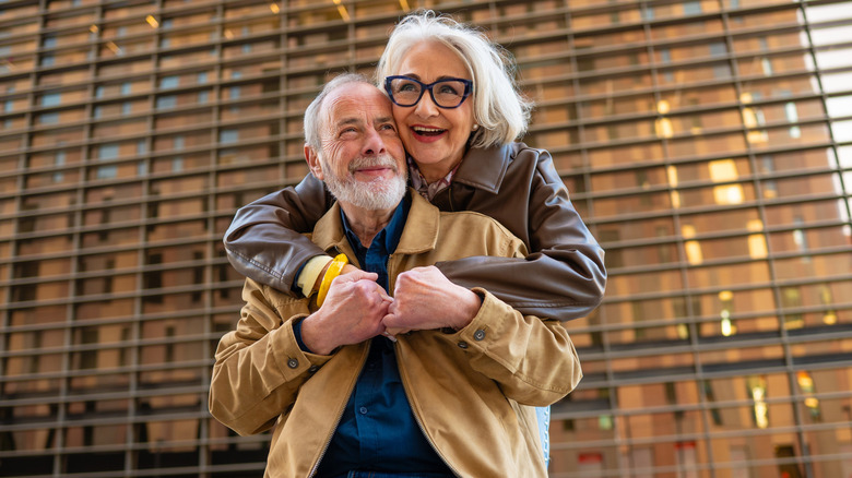An older couple embraces smiling in front of a building