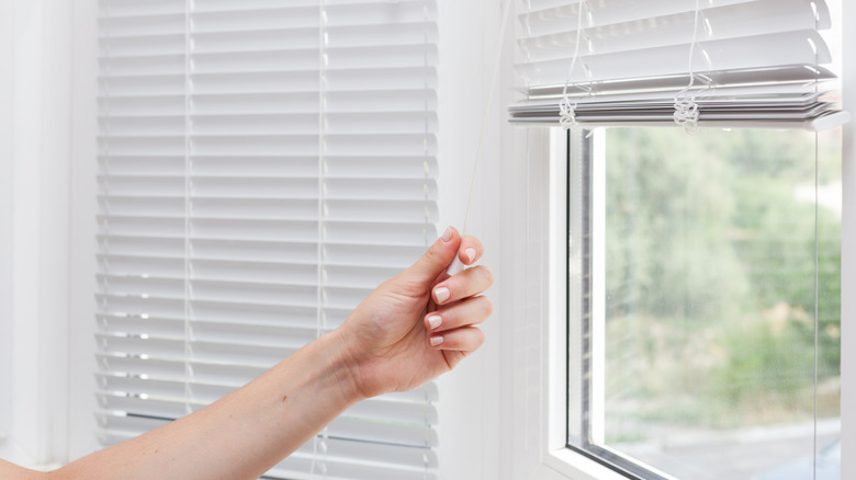 Person pulling the cord on some basic white blinds