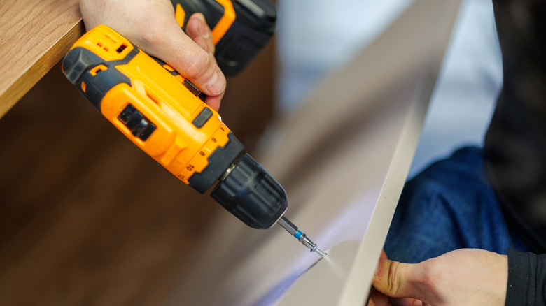 Close-up of person assembling furniture with a cordless drill