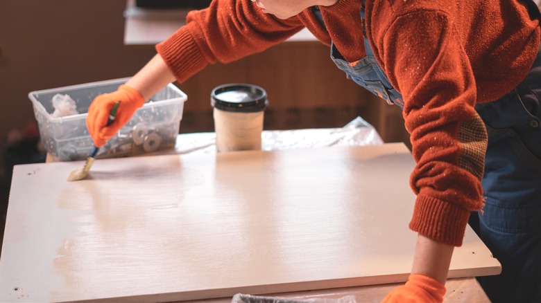 Woman polishing DIY wood table surface for custom table build in covered workspace