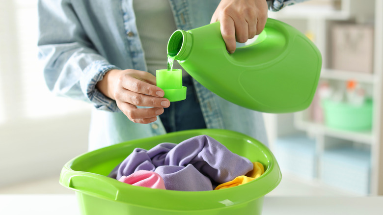 A woman pours laundry detergent from the bottle into the cap.