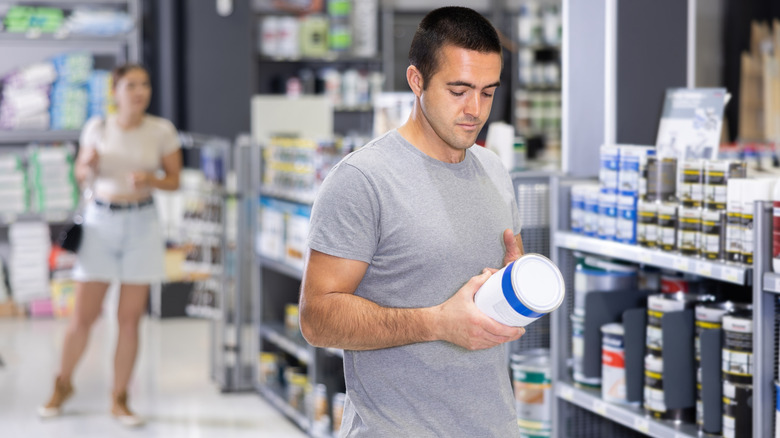 a man looks at a small can of paint at a hardware store