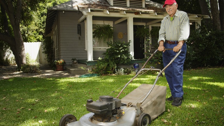 Older man pushing lawnmower in front of house