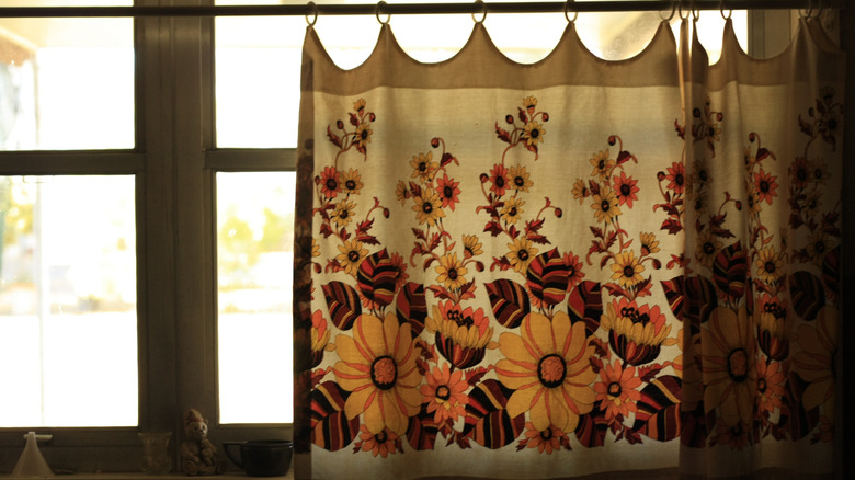 A cafe curtain in kitchen window with colorful flowers on it