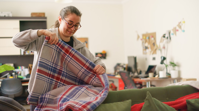 A woman folding plaid blanket in her living room