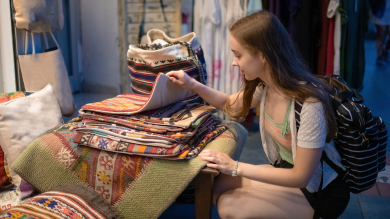A young woman looking through a pile of patterned rugs