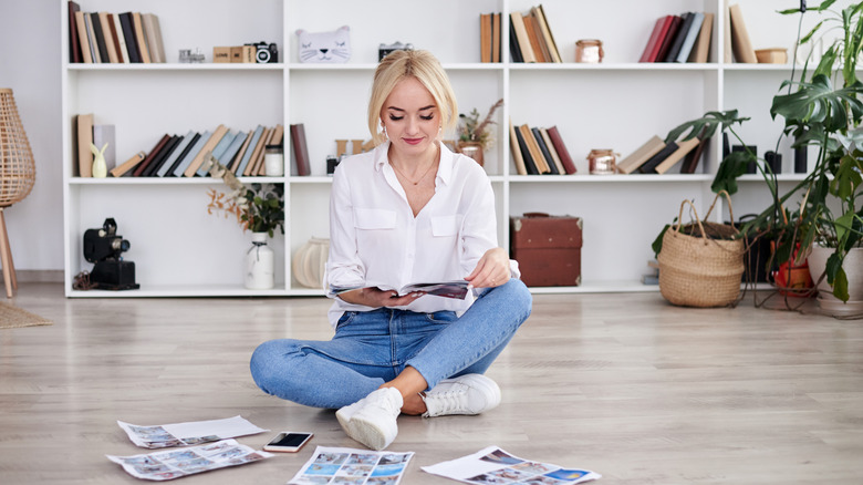 A woman sits on the floor reading a magazine with several other open magazines in front of her