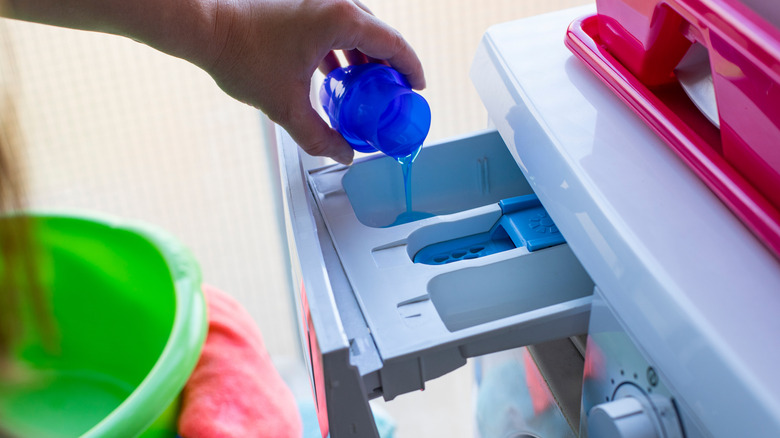 Hand pouring laundry detergent in washing machine dispenser