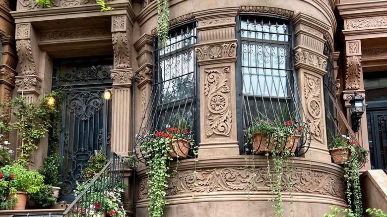Ornate brownstone facade with lush, potted plants and flowers growing in its window boxes and on the stoop in Harlem, New York City