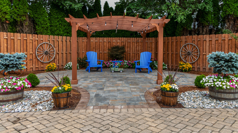 A backyard patio with a variety of pavers, with a wooden pergola and attractive flowers.
