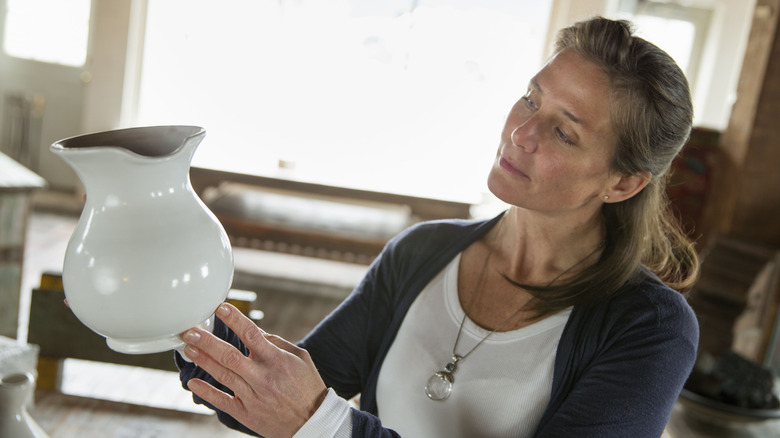 A woman holds a white jug in an antique store