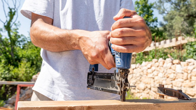A man uses a nail gun on a wood board