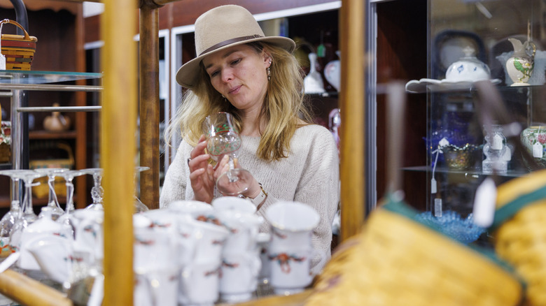 A woman wearing a hat shops for dishes and glasses at a store.