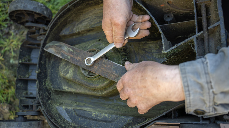 A close-up of a man removing a lawn mower blade