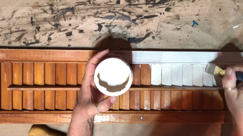 A woman paints a wood shutter white