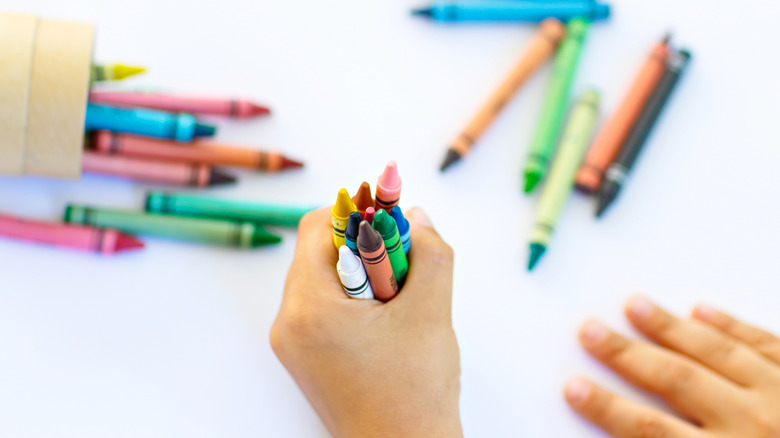Hand fisting colorful crayons over a white surface