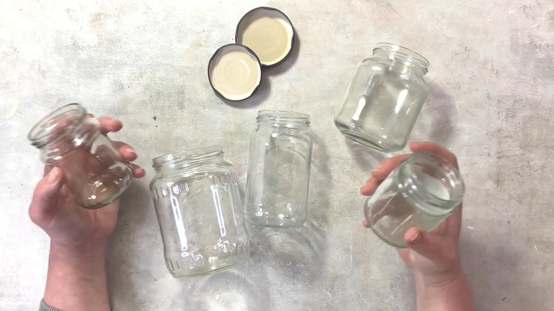 Person holding various empty glass jars from kitchen over gray concrete surface
