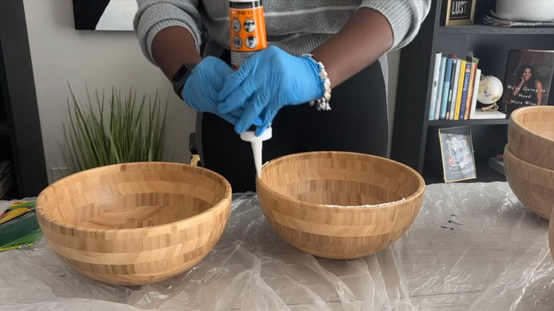 Young woman gluing IKEA salad bowls together for DIY over plastic tarp-covered table