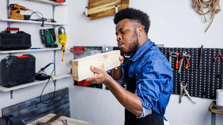 A young man blows dust off a piece of scrap wood while working on a DIY project