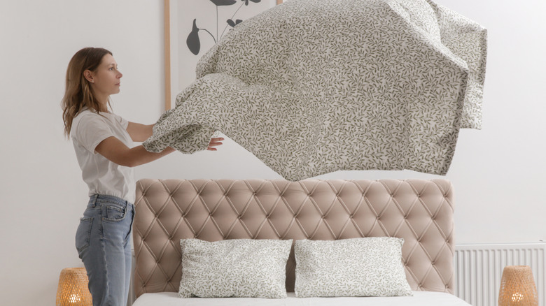 A woman putting a new sheet on the bed.