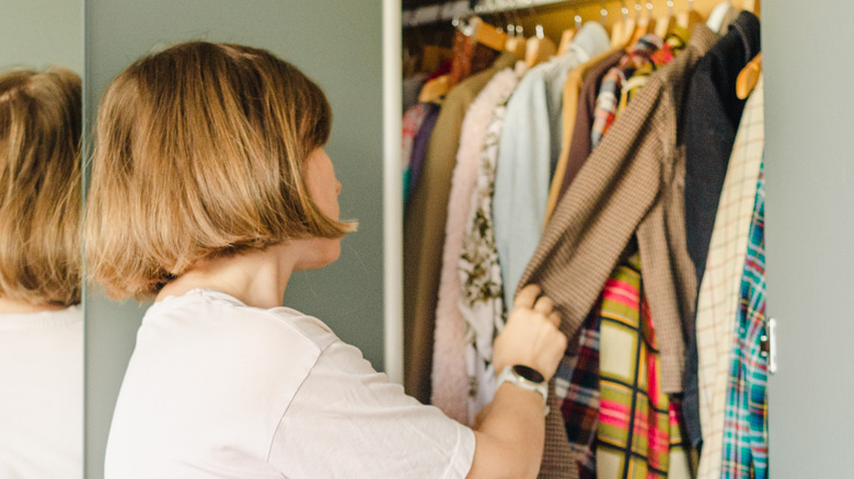 Woman standing in front of open closet organizing clothes
