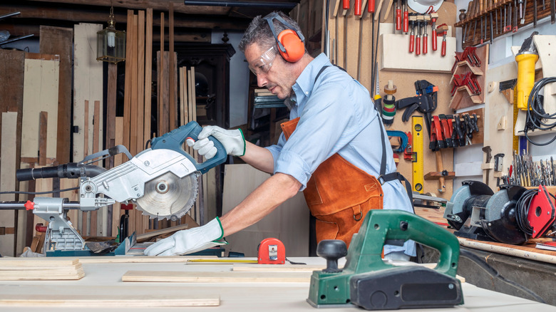 Person with work gloves and goggles cutting wood boards in a garage.