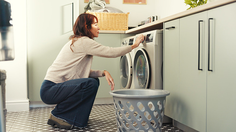 A young woman turns on a washing machine.