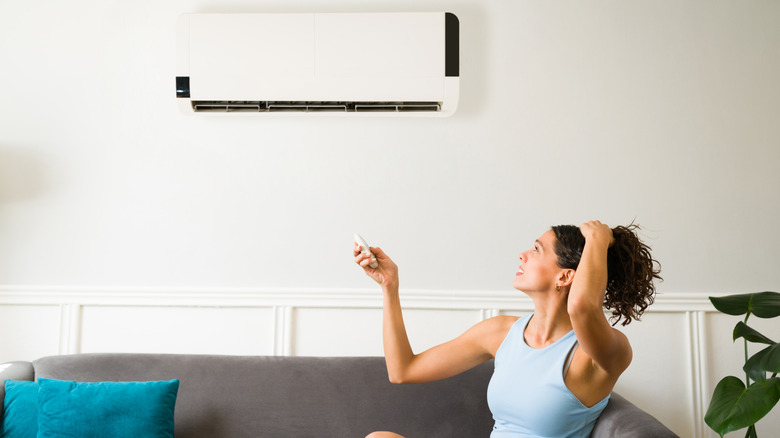 A woman is sitting on a couch and turning on the AC with a remote in her hand