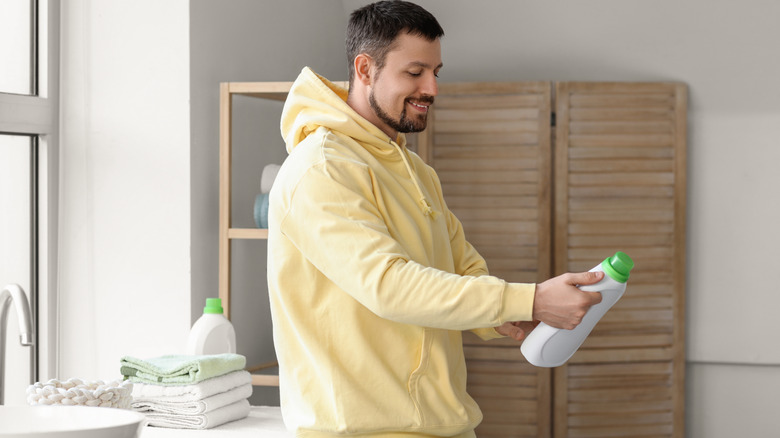 Man looking at laundry detergent bottle while standing in bathroom