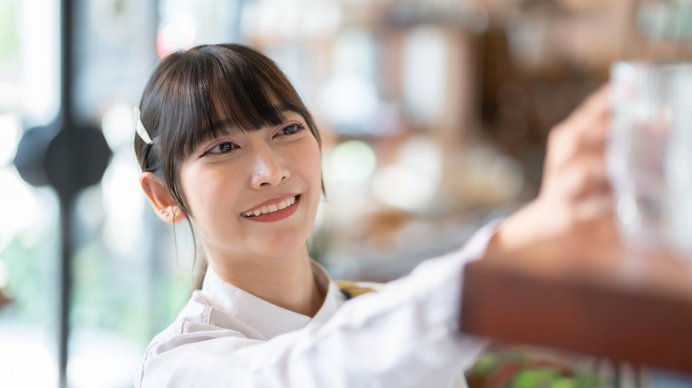 A woman reaching for glassware in a store