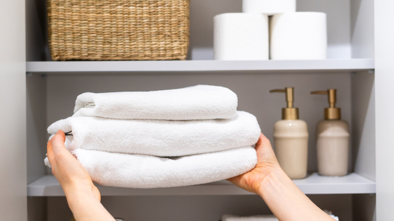 Hands putting towels in a cabinet with other bathroom essentials