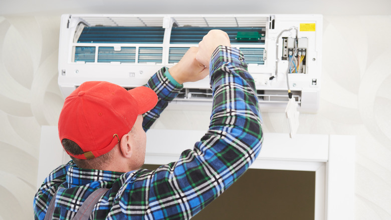 A person wearing a plaid shirt and an orange-red hat repairing an air conditioner indoor unit