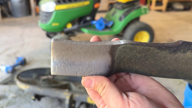Person holding dull and pitted lawn mower blade in need of sharpening