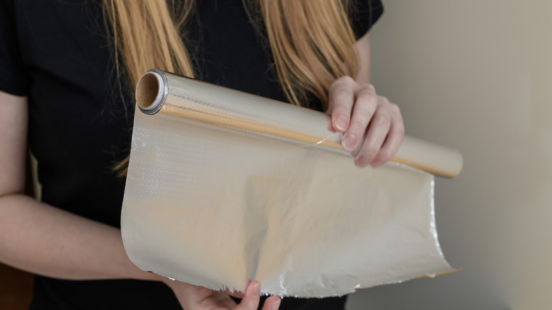 A woman holds a roll of aluminum foil