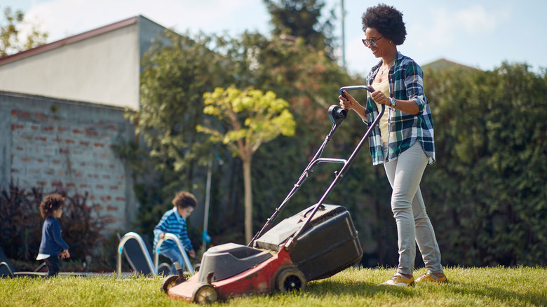 A woman mowing the lawn with her kids in the background