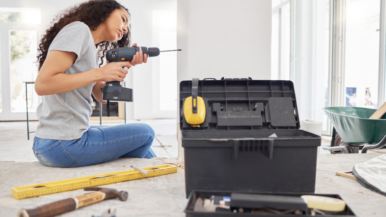Woman holding a drill with a toolbox and other tools in the foreground