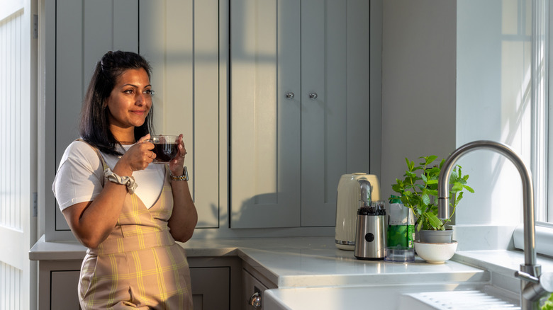 A woman holding a cup of coffee in a tidy kitchen.