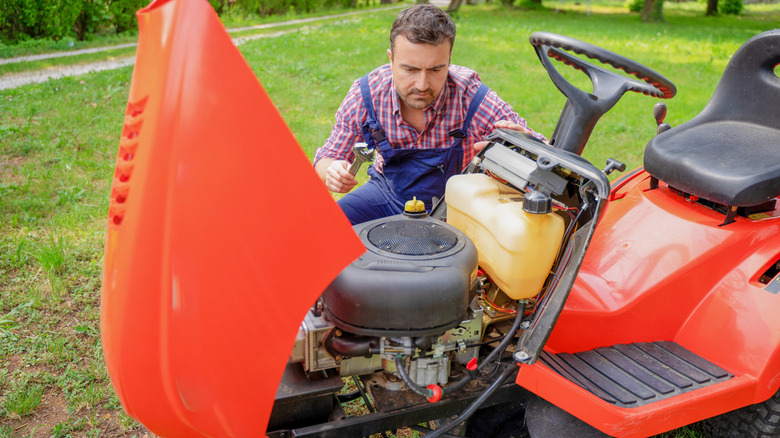 Man inspecting a broken riding lawn mower