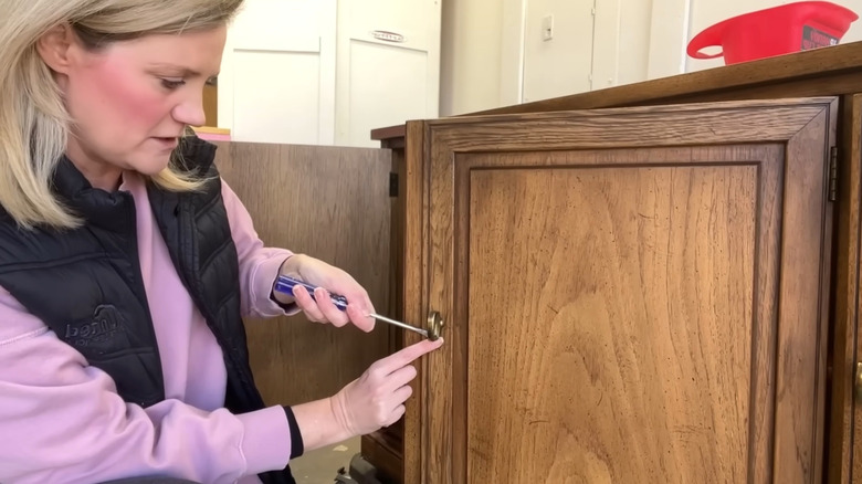 A woman takes the hinges off a vintage hutch