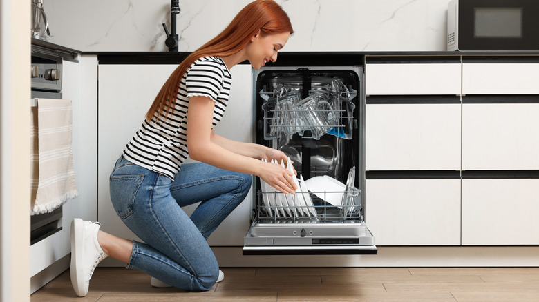 A smiling woman is loading dishes in a dishwasher